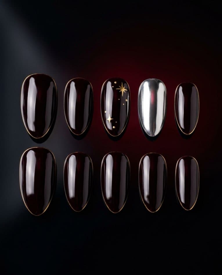 A complete set of deep black-cherry press-on nails with gold star accents and one mirror chrome nail